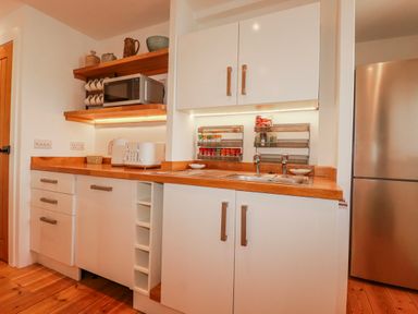A kitchen with a microwave, sink, and shelves at Logan Barn in Poldue near Camelford