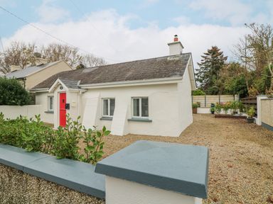 A small white house with a red door and a gravel driveway at Bayside Cottage in Rosslare Strand County Wexford
