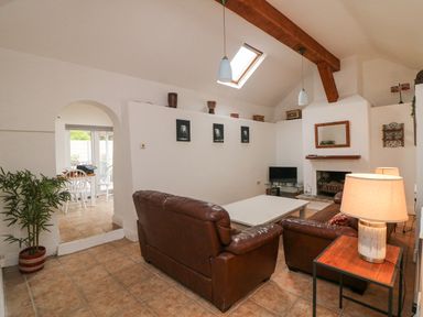 A living room with brown leather sofas a white coffee table a fireplace and a small TV next to an arched doorway at Bayside Cottage in Rosslare Strand County Wexford