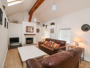 A living room with brown leather sofas a white coffee table a fireplace a TV on a glass stand lamps and a wall clock at Bayside Cottage Rosslare Strand County Wexford