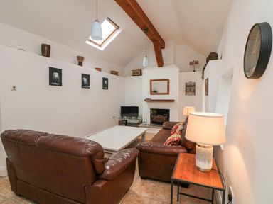 A living room with brown leather sofas a white coffee table a fireplace a TV and a wooden beam on the ceiling at Bayside Cottage in Rosslare Strand County Wexford
