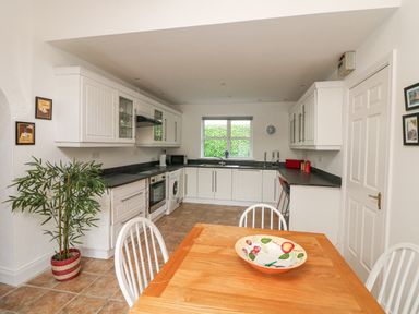 A kitchen with white cabinets a wooden dining table with white chairs and a decorative bowl at Bayside Cottage in Rosslare Strand County Wexford