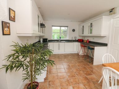 A kitchen with white cabinets black countertops a window a clock and two bar stools at Bayside Cottage in Rosslare Strand County Wexford