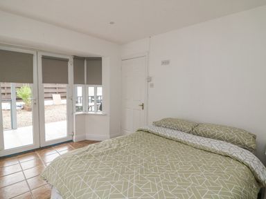 A bedroom with a bed and patterned bedding near glass doors and a window at Bayside Cottage in Rosslare Strand County Wexford