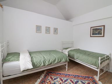 A bedroom with two single beds with green bedding and framed pictures on white walls at Bayside Cottage in Rosslare Strand County Wexford