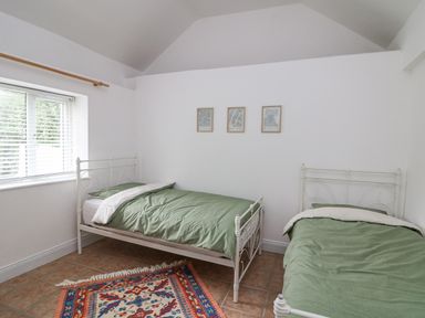 A bedroom with two single beds with green bedding a window with blinds and a colorful rug on the floor at Bayside Cottage in Rosslare Strand County Wexford