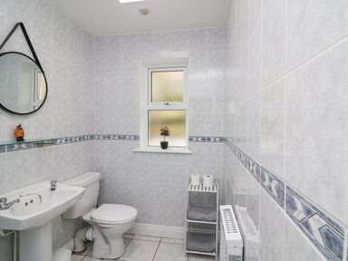A bathroom with a toilet sink mirror small window and shelf holding towels and toilet paper at Bayside Cottage in Rosslare Strand County Wexford