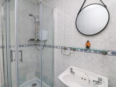 A bathroom with a glass shower enclosure a round mirror a sink and a small figurine on a glass shelf at Bayside Cottage in Rosslare Strand County Wexford
