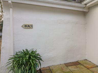 A white wall with a small sign saying beach and a green potted plant on a tiled floor at Bayside Cottage in Rosslare Strand County Wexford