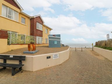 A pathway leading to a beach with a bench and a house on the left and a wooden fence on the right at Bayside Cottage in Rosslare Strand County Wexford