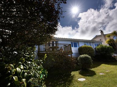 A house with a wooden deck and outdoor furniture surrounded by bushes and trees at Northern Lights in Polzeath