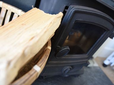 A close up of a wood burning stove and a wicker basket with firewood at Northern Lights in Polzeath