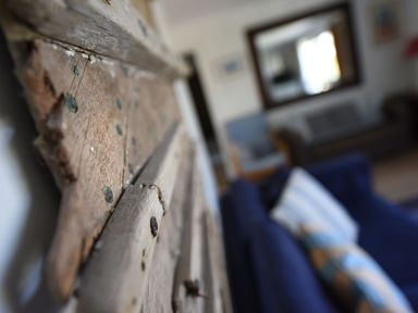Close up of a wooden wall decoration with a living room featuring sofas and a large mirror in the background at Northern Lights in Polzeath