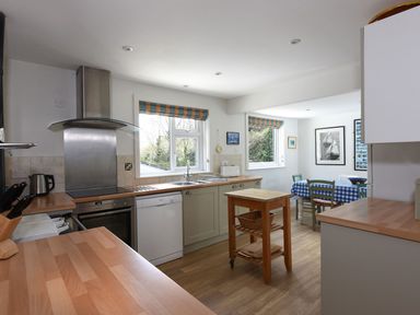 A kitchen with wooden counters a small wooden island and a dining area with a table covered with a checked cloth at Northern Lights in Polzeath