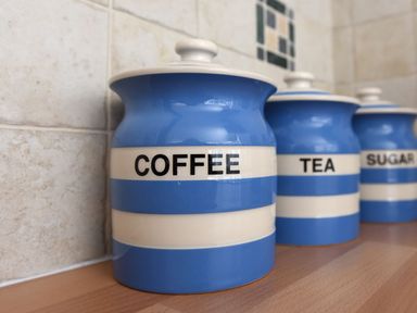 Three blue and white striped canisters labeled coffee tea and sugar on a wooden countertop in a kitchen