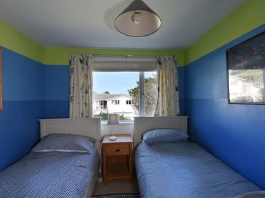 A bedroom with two single beds separated by a wooden nightstand under a window with patterned curtains at Northern Lights Polzeath