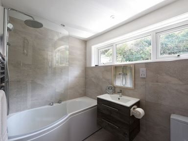 A bathroom with a bathtub shower combination sink with cabinet and a window at Northern Lights in Polzeath