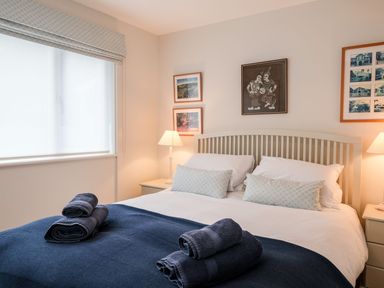A bedroom with a double bed with folded towels on a blanket and framed pictures on the wall at Northern Lights in Polzeath