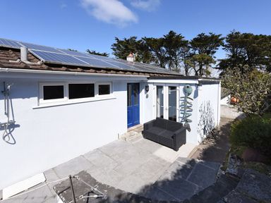 A patio area with a black outdoor sofa and blue door on a white house with solar panels on the roof at Northern Lights in Polzeath