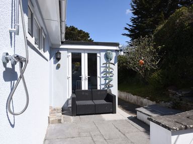 An outdoor patio area with a black wicker loveseat a wall-mounted shower and a glass double door at Northern Lights in Polzeath