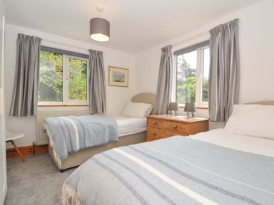 A bedroom with two beds, a bedside table and windows at Seaworthy in Daymer Bay
