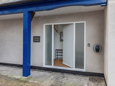 An entrance door open with a shoe rack visible inside and a blue painted post outside at Groves House in Castletown near Fortuneswell