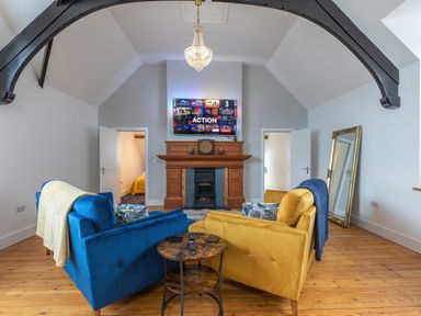 A living room with blue and yellow sofas facing a wooden fireplace and a wall-mounted TV at Groves House Castletown near Fortuneswell