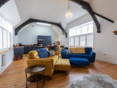 A living room with yellow and blue sofas a round side table wooden floor and an open kitchen with navy cabinets at Groves House Castletown near Fortuneswell