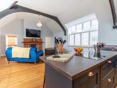 An open living room and kitchen area with a blue sofa wooden floor and a kitchen island with cooking utensils at Groves House in Castletown near Fortuneswell