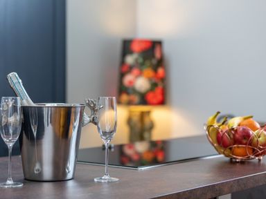 A kitchen counter with a metal ice bucket and champagne glasses next to a fruit basket and a floral lamp in the background at Groves House Castletown near Fortuneswell