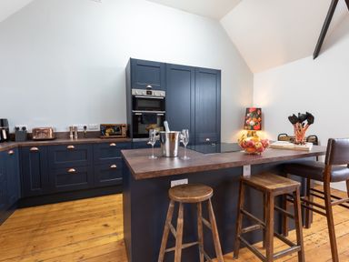 A kitchen with dark blue cabinets wooden stools a countertop with a fruit bowl and kitchen utensils at Groves House Castletown near Fortuneswell