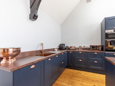 A kitchen with blue cabinets copper sink and appliances on wooden floor at Groves House in Castletown near Fortuneswell