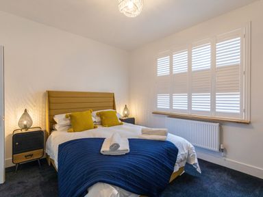 A bedroom with a bed featuring a mustard headboard blue blanket yellow pillows and two bedside tables with lamps at Groves House in Castletown near Fortuneswell