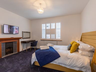 A bedroom with a yellow bed and blue blanket a desk and chair near a window with shutters at Groves House in Castletown near Fortuneswell