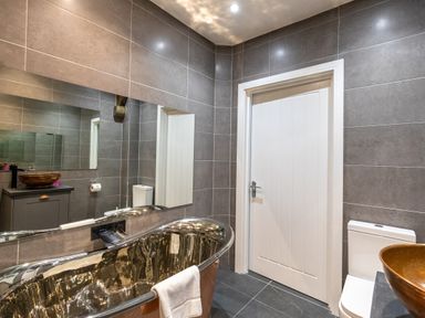 A bathroom with a copper bathtub a white door a toilet and a cabinet with a copper sink at Groves House in Castletown near Fortuneswell