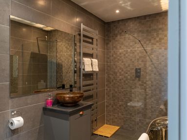 A bathroom with a round sink on a vanity unit a towel rail with towels a walk in shower with tiled walls and a wooden mat on the floor at Groves House Castletown near Fortuneswell