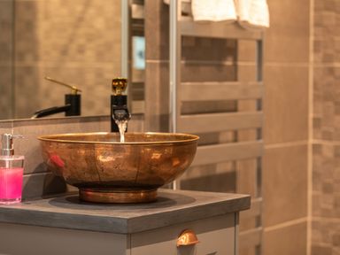 A bathroom sink with a copper basin and running water on a countertop with a soap dispenser and towel rack at Groves House in Castletown near Fortuneswell