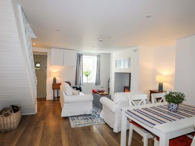 A living room with white sofas, a coffee table, a dining table, lamps, and a fireplace at Cwrt in Dwyran near Niwbwrch Newborough
