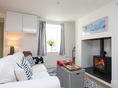 A living room with white sofa and blue cushions next to a window and a fireplace with fire burning at Cwrt Dwyran near Niwbwrch Newborough