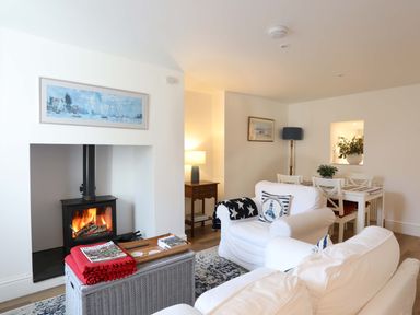 A living room with a wood burning stove a white sofa and armchair a dining table with chairs and framed paintings on the walls at Cwrt in Dwyran near Niwbwrch Newborough
