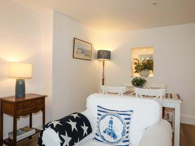 A living room with a white armchair, side table with lamp, dining table with chairs and plants at Cwrt in Dwyran near Niwbwrch Newborough