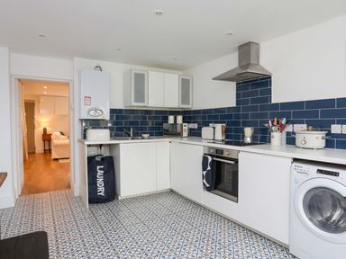 A kitchen with white cabinets blue tiled backsplash patterned floor and various appliances including a washing machine at Cwrt in Dwyran near Niwbwrch Newborough
