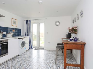 A kitchen with a washing machine oven wooden table blue and white tiles and double glass doors at Cwrt in Dwyran near Niwbwrch Newborough