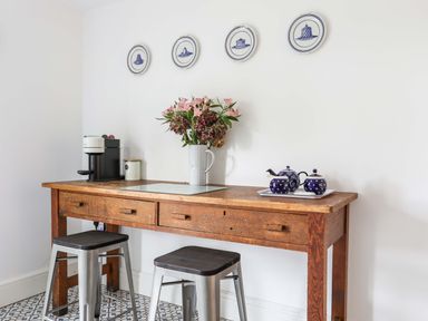 A wooden table with a flower vase, teapot set, coffee machine and two stools at Cwrt in Dwyran near Niwbwrch Newborough