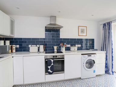 A kitchen with white cabinets blue tile backsplash and patterned floor at Cwrt in Dwyran near Niwbwrch Newborough
