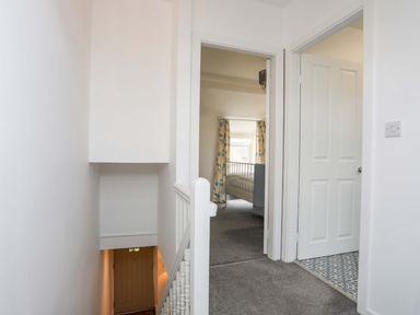 A hallway with carpeted floor leading to a bedroom and a room with patterned tile flooring at Cwrt Dwyran near Niwbwrch Newborough