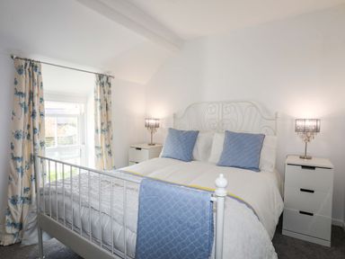 A bedroom with a white metal bed frame blue pillows and lamps on bedside tables at Cwrt in Dwyran near Niwbwrch Newborough
