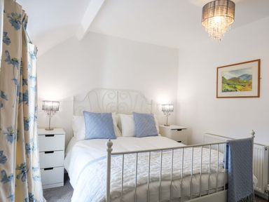 A bedroom with a white metal bed frame blue pillows and floral curtains at Cwrt in Dwyran near Niwbwrch Newborough