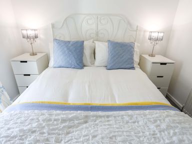 A bedroom with a bed with blue pillows white bedding and two bedside tables with lamps at Cwrt in Dwyran near Niwbwrch Newborough