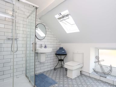A bathroom with a shower, toilet, sink, towel stack, round mirror, skylight, and decorative anchor at Cwrt in Dwyran near Niwbwrch Newborough